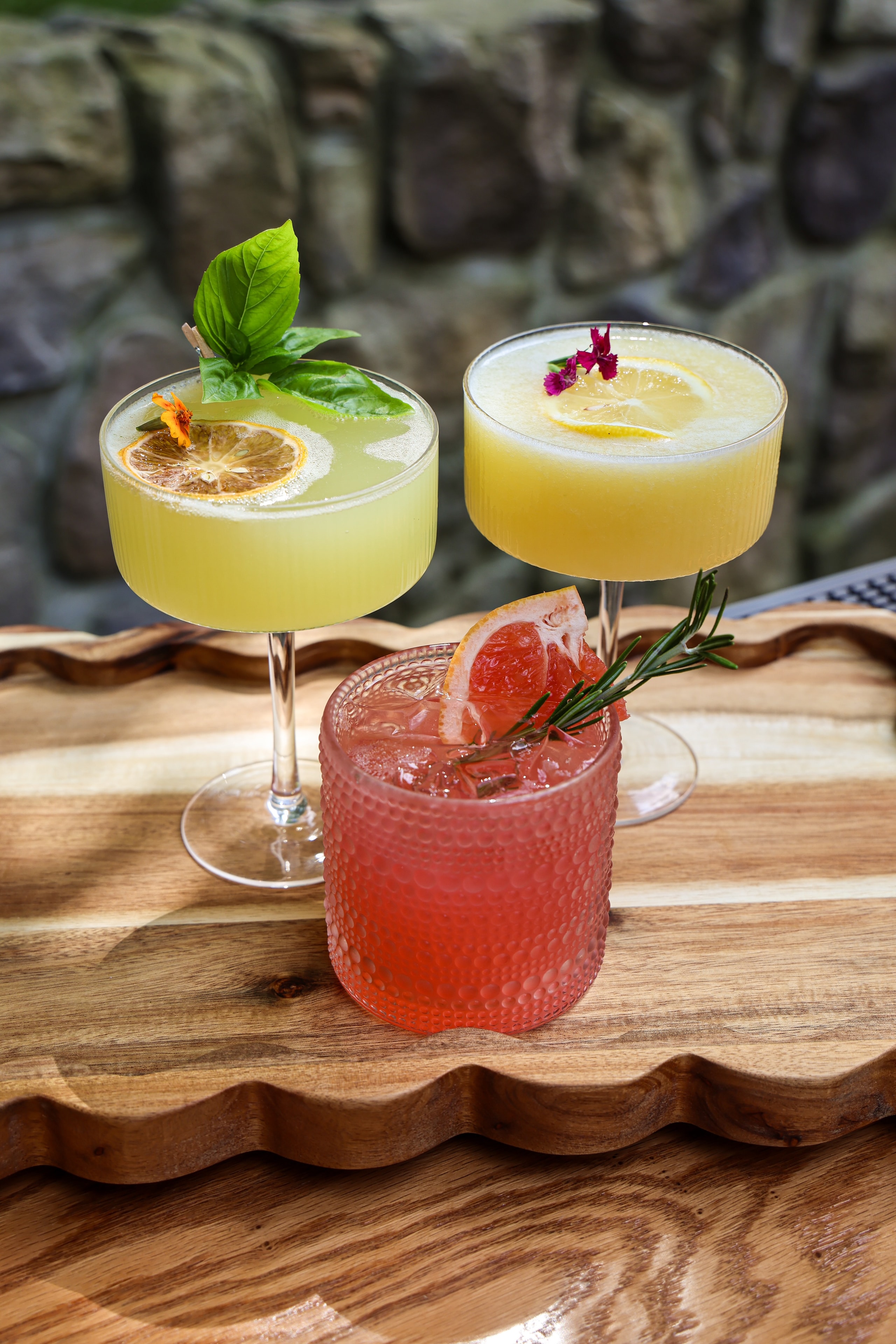 Three colorful cocktails on wooden board garnished